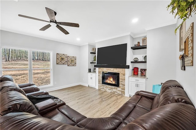 living room featuring built in shelves, ornamental molding, ceiling fan, a fireplace, and light hardwood / wood-style floors