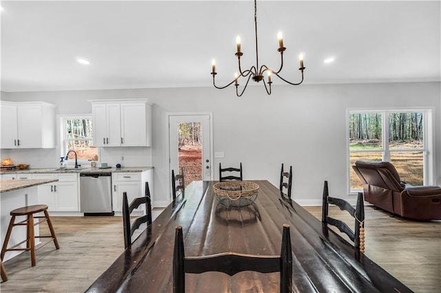 dining space with ornamental molding, a chandelier, sink, and light hardwood / wood-style flooring