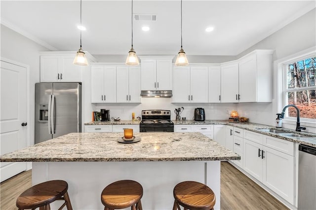 kitchen featuring appliances with stainless steel finishes, decorative light fixtures, sink, and a kitchen island