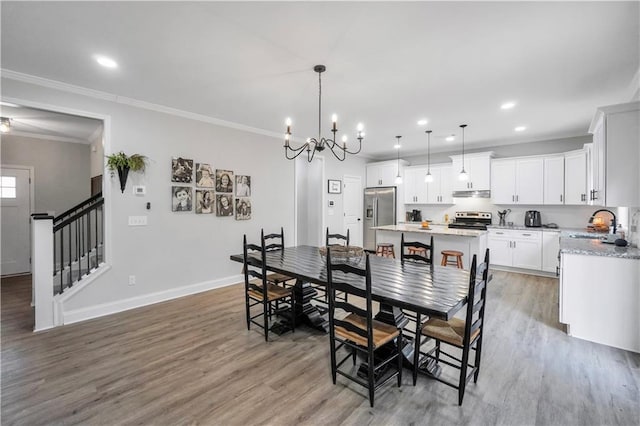 dining space with wood-type flooring, ornamental molding, sink, and a notable chandelier