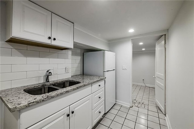 kitchen featuring white refrigerator, light stone countertops, sink, and white cabinets