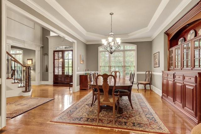 dining room featuring healthy amount of natural light, a raised ceiling, a chandelier, stairway, and crown molding