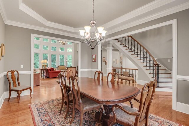 dining room with a chandelier, ornamental molding, light wood-type flooring, a tray ceiling, and stairway