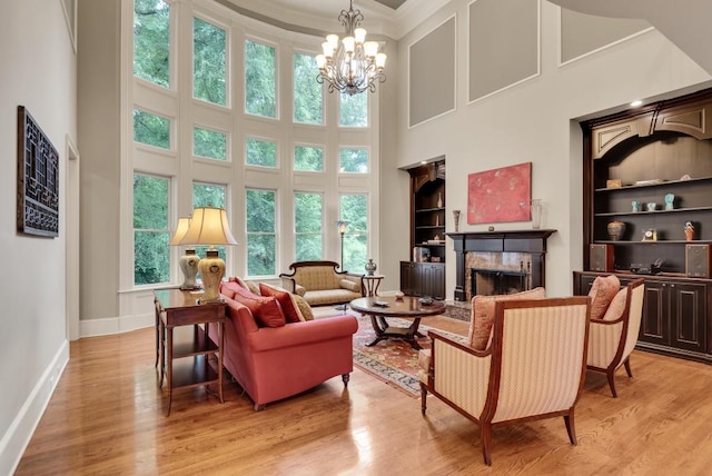 living room with built in features, a high ceiling, a fireplace, light wood-type flooring, and baseboards