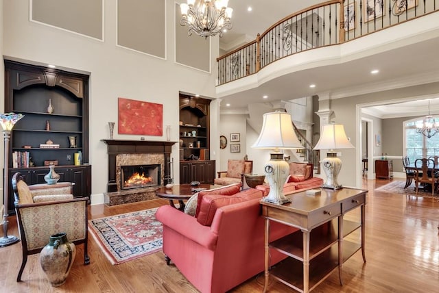 living room featuring a chandelier, crown molding, built in shelves, wood finished floors, and a high end fireplace