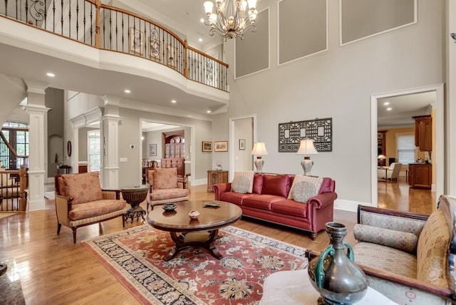 living room with decorative columns, a high ceiling, ornamental molding, light wood-style floors, and recessed lighting
