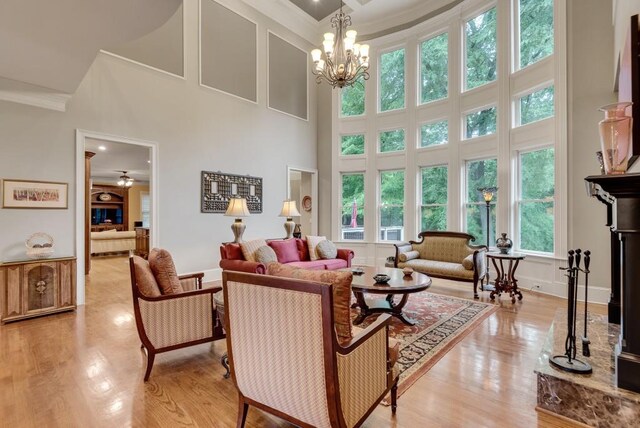 living room with ornamental molding, a towering ceiling, light wood finished floors, baseboards, and a chandelier