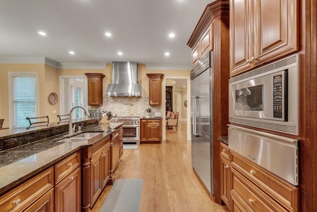 kitchen featuring wall chimney range hood, a sink, built in appliances, a warming drawer, and ornamental molding