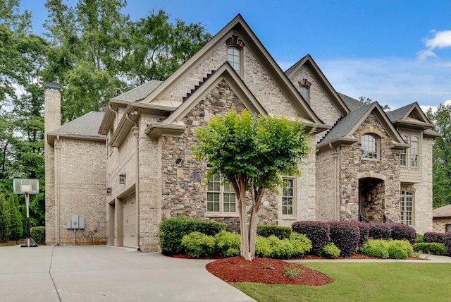 french country inspired facade with concrete driveway, a chimney, a garage, a shingled roof, and stone siding