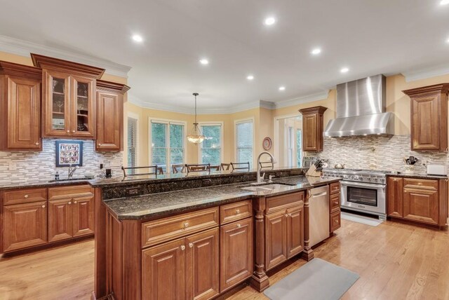 kitchen featuring wall chimney exhaust hood, stainless steel appliances, a sink, light wood-style flooring, and brown cabinets