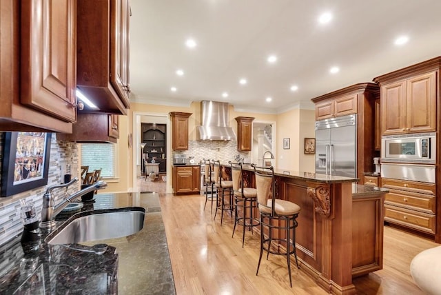 kitchen featuring built in appliances, wall chimney exhaust hood, a sink, crown molding, and a warming drawer