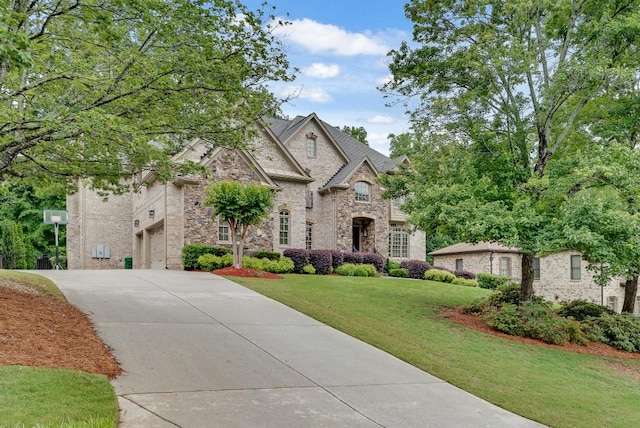 french country style house featuring stone siding, driveway, a front yard, and an attached garage