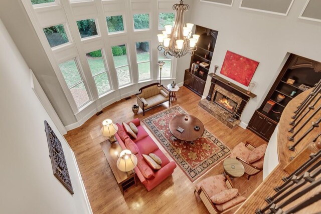 living area featuring wood finished floors, a fireplace, a towering ceiling, a chandelier, and baseboards