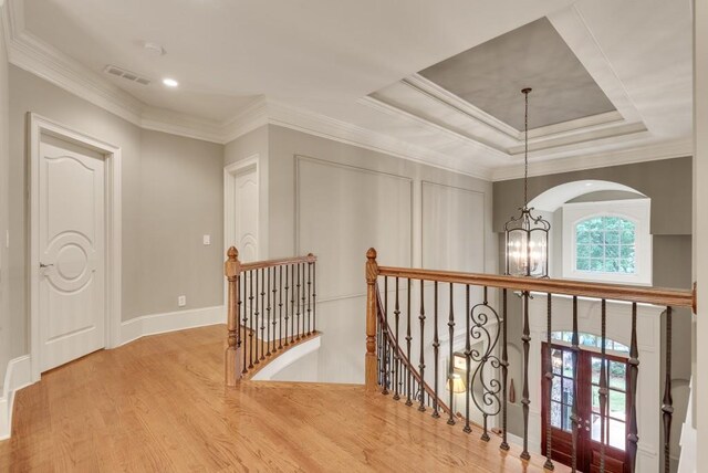hallway with an upstairs landing, a chandelier, wood finished floors, crown molding, and baseboards