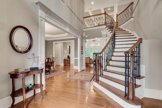 entrance foyer featuring crown molding, stairs, light wood-type flooring, decorative columns, and a towering ceiling