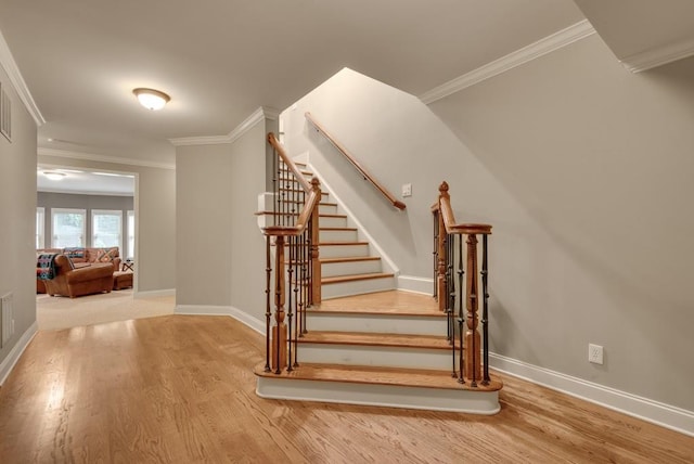 staircase featuring wood finished floors, baseboards, and crown molding