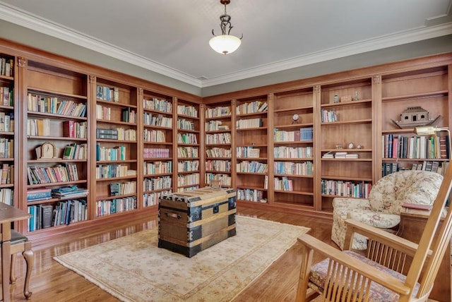 living area with bookshelves, ornamental molding, and wood finished floors