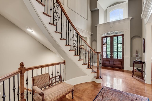 foyer with healthy amount of natural light, a towering ceiling, wood finished floors, french doors, and stairway