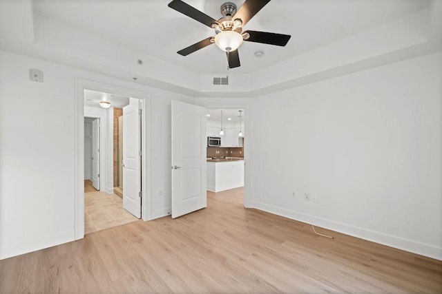 spare room featuring light wood-style floors, baseboards, visible vents, and a raised ceiling