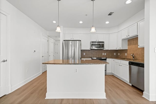 kitchen featuring tasteful backsplash, dark stone counters, a kitchen island, appliances with stainless steel finishes, and a sink