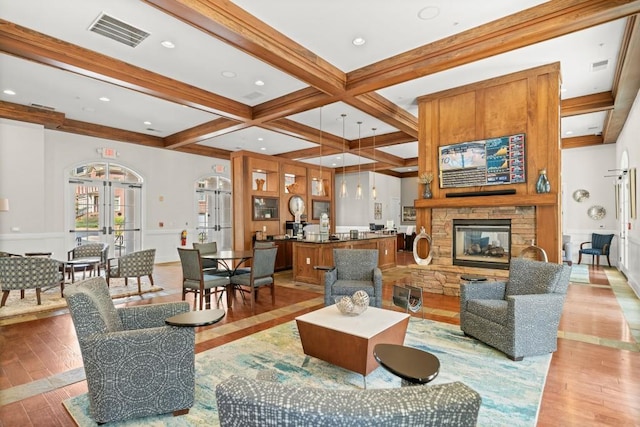 living area with a fireplace, visible vents, light wood-style floors, french doors, and beamed ceiling