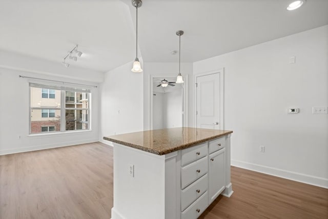 kitchen featuring baseboards, dark stone counters, a center island, hanging light fixtures, and light wood-type flooring