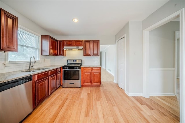 kitchen with appliances with stainless steel finishes, sink, light stone counters, and light wood-type flooring