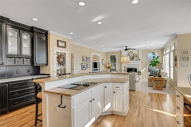 kitchen featuring a center island, black electric stovetop, a breakfast bar area, a fireplace, and light wood-style floors