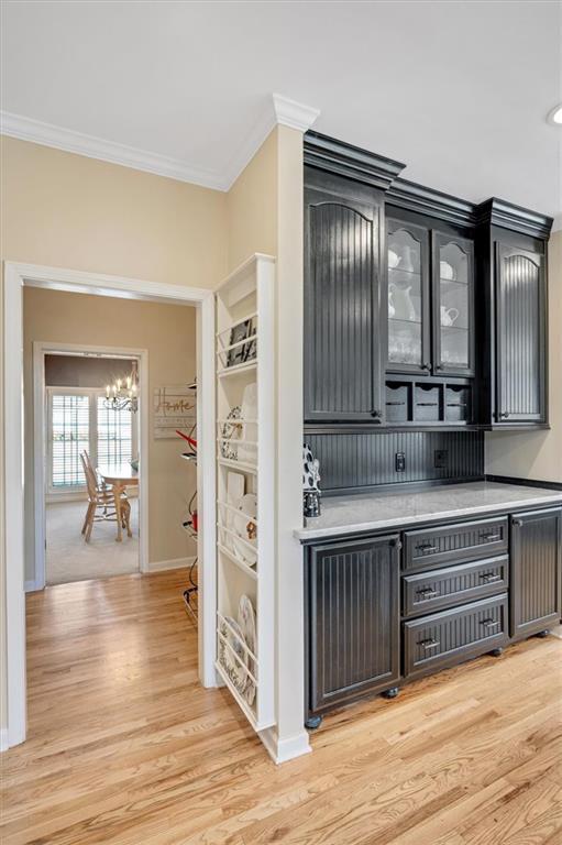 bar with light wood-type flooring, baseboards, a notable chandelier, and crown molding