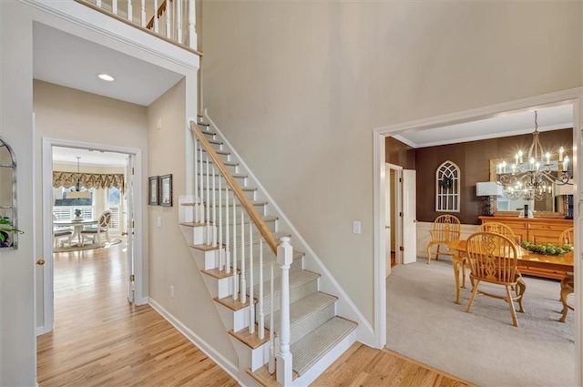 stairway with a notable chandelier, a high ceiling, baseboards, and wood finished floors