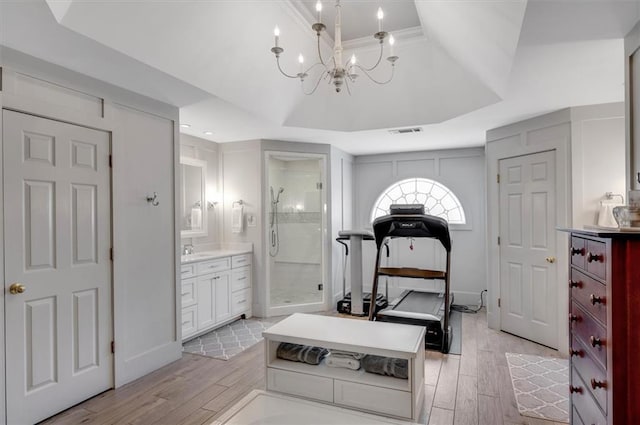 exercise room with visible vents, light wood-style flooring, and a tray ceiling