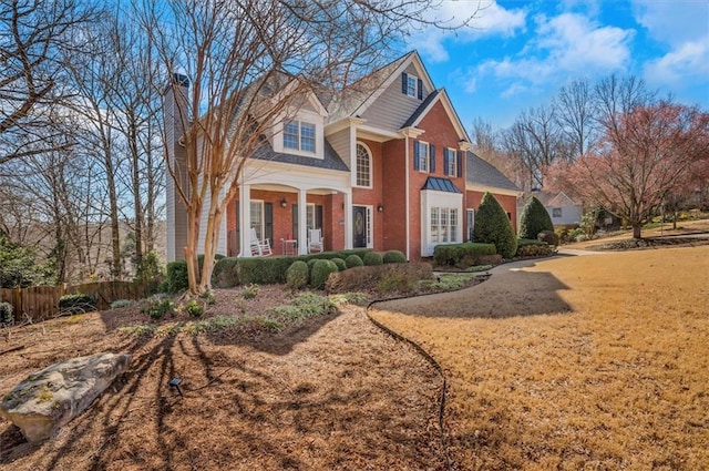 view of front of home featuring fence, covered porch, a chimney, a front lawn, and brick siding