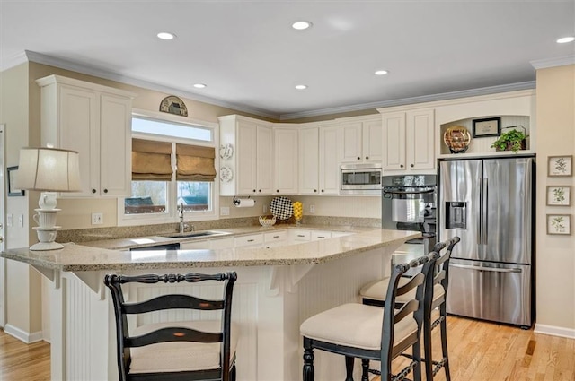 kitchen featuring crown molding, light stone countertops, appliances with stainless steel finishes, a peninsula, and a sink