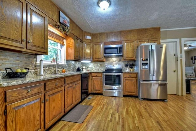 kitchen featuring light stone countertops, appliances with stainless steel finishes, a textured ceiling, decorative backsplash, and light hardwood / wood-style flooring