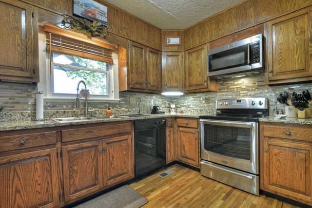 kitchen with light stone countertops, appliances with stainless steel finishes, sink, light wood-type flooring, and a textured ceiling