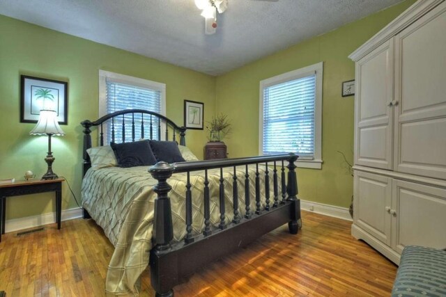 bedroom featuring hardwood / wood-style floors, multiple windows, a textured ceiling, and ceiling fan