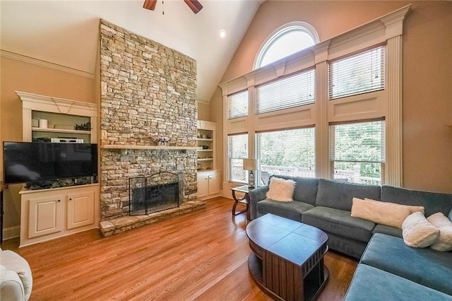 living room with hardwood / wood-style floors, ceiling fan, high vaulted ceiling, built in shelves, and a stone fireplace