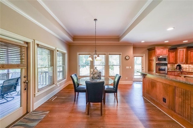 dining space featuring crown molding, a raised ceiling, dark hardwood / wood-style flooring, and an inviting chandelier