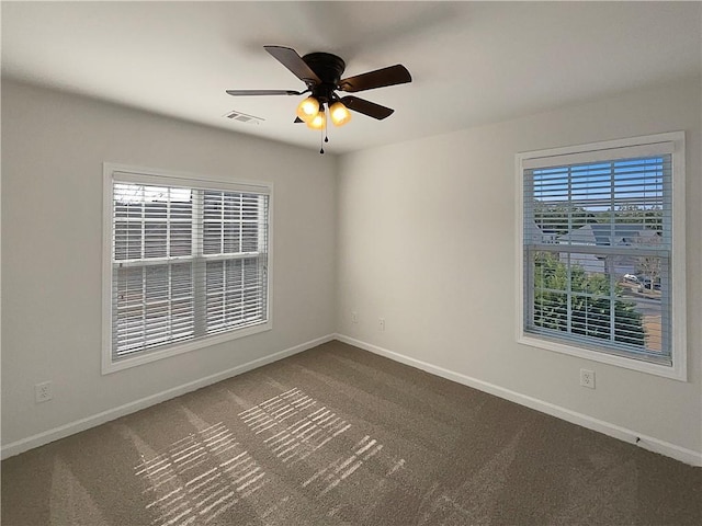 empty room with a wealth of natural light, visible vents, dark carpet, and baseboards