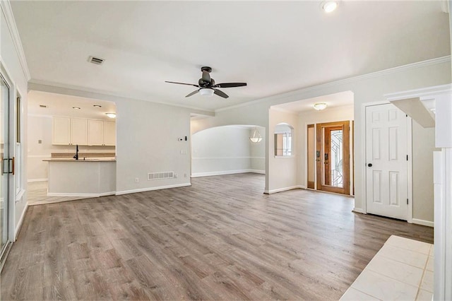 unfurnished living room with ornamental molding, ceiling fan, light wood-type flooring, baseboards, and arched walkways