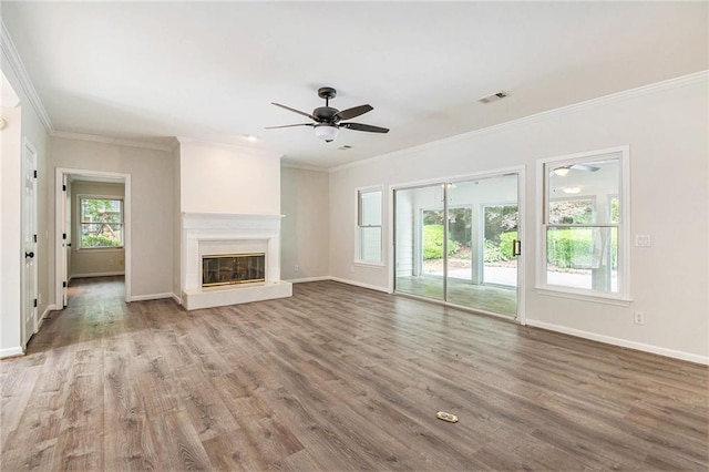 unfurnished living room with ceiling fan, baseboards, wood finished floors, ornamental molding, and a glass covered fireplace