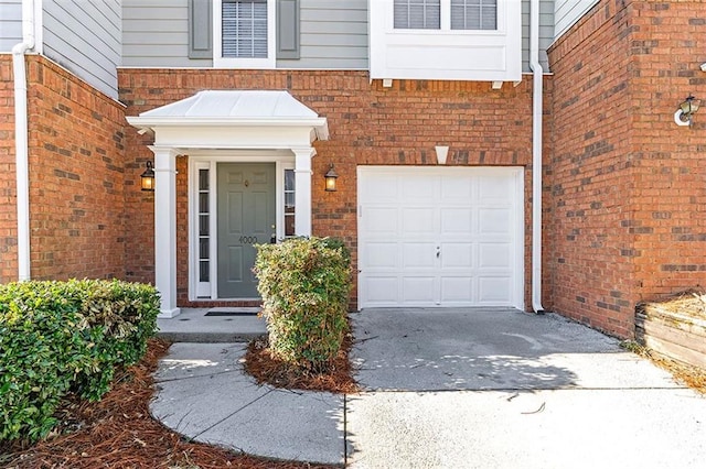 doorway to property with an attached garage, brick siding, and driveway