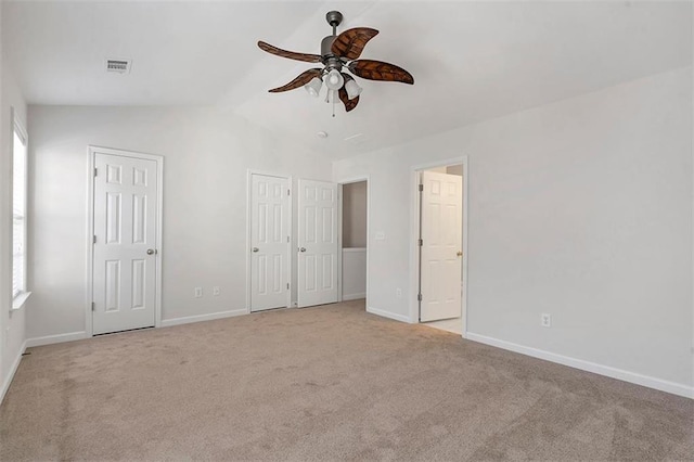 unfurnished bedroom featuring visible vents, light carpet, two closets, lofted ceiling, and baseboards