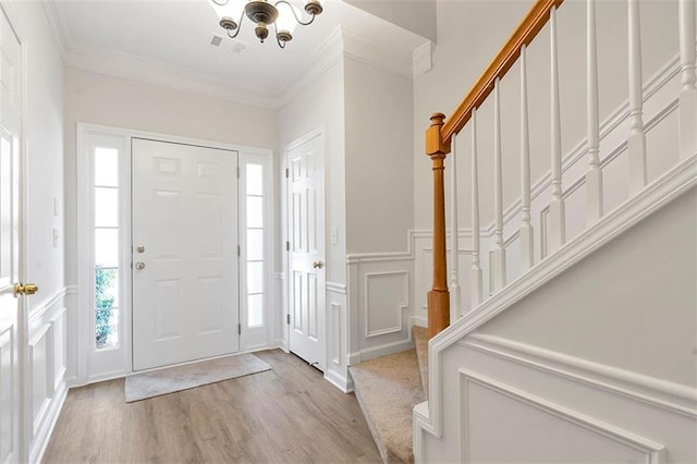 foyer with visible vents, crown molding, stairs, and a decorative wall