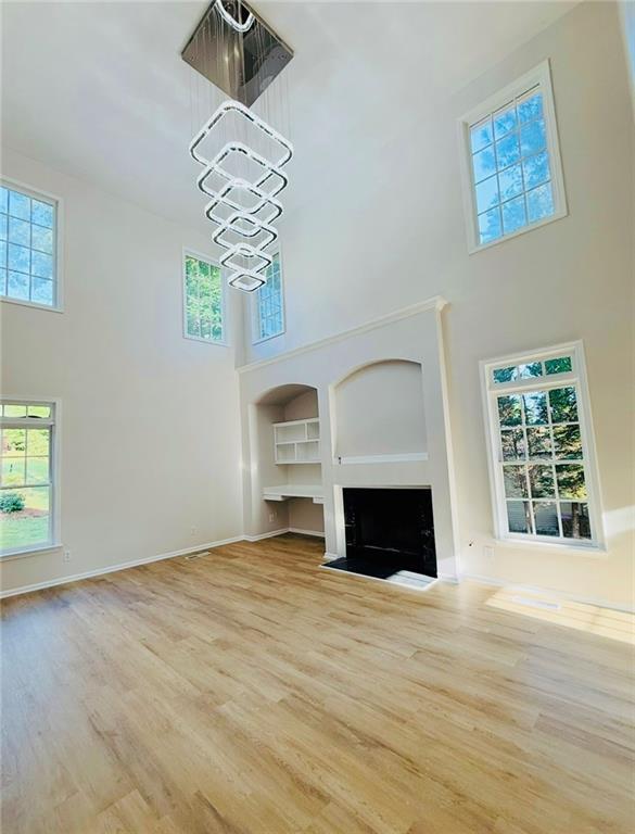 10950 Glenhurst, Duluth, GA 30097 - unfurnished living room with a towering ceiling, a chandelier, wood finished floors, and a fireplace with flush hearth