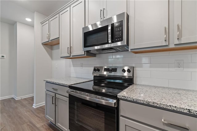 kitchen with light stone counters, decorative backsplash, stainless steel appliances, and wood-type flooring