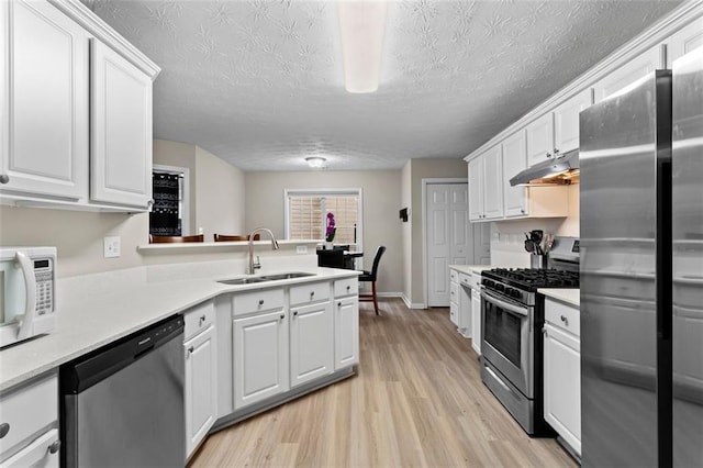 kitchen with a sink, under cabinet range hood, white cabinetry, appliances with stainless steel finishes, and light countertops