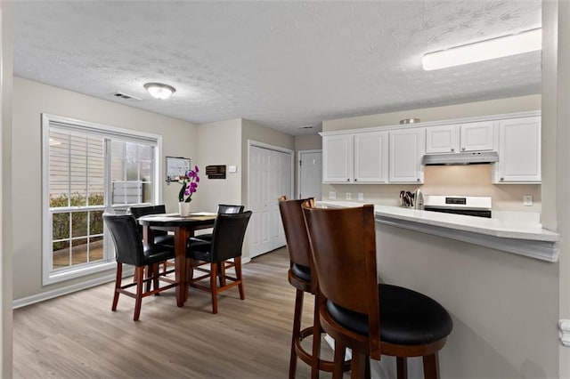 kitchen with visible vents, under cabinet range hood, white cabinets, light countertops, and stove