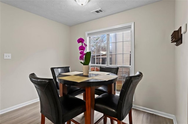 dining space featuring visible vents, a textured ceiling, baseboards, and wood finished floors