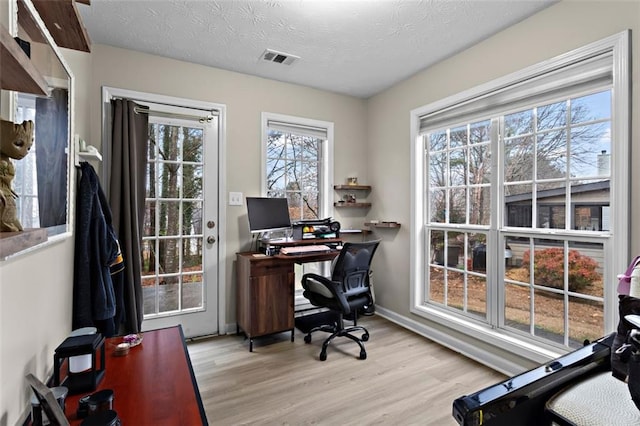 office area with baseboards, visible vents, a textured ceiling, and light wood-style floors